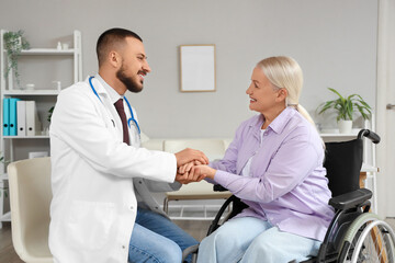 Obraz premium Male doctor with mature woman in wheelchair holding hands at hospital
