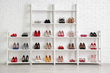 Shelves with stylish women's shoes near white brick wall in room