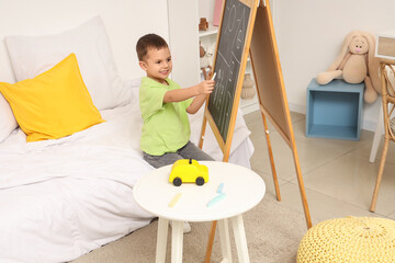 Cute little boy drawing on chalkboard in bedroom