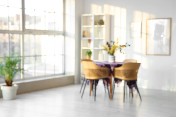 Interior of dining room with beautiful flowers and stylish purple cloth on table near window, blurred view