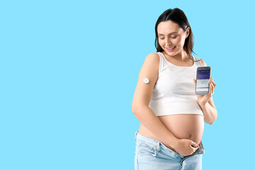 Young pregnant woman with glucose sensor and mobile phone on blue background. Gestational diabetes...
