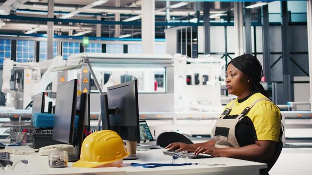 Engineer configures solar panel systems on PC in modern factory, working on energy optimization software. Expert manages photovoltaic operations in a high tech, automated facility. Camera A.