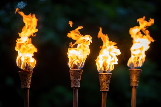 Four tiki torches burning brightly at night in a tropical garden setting close up shot with blurred background