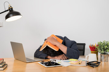 Working late in the office. Stressed young man sitting at a table among books. Overworked guy...
