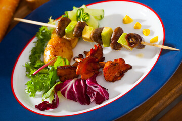 Grilled chicken hearts with avocado on skewers served with vegetables and fried chanterelles on blue plate