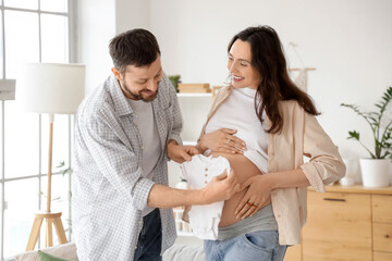 Happy pregnant couple with baby bodysuit at home