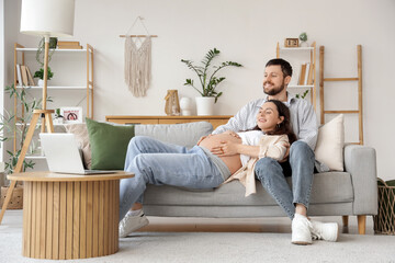 Obraz premium Happy pregnant couple resting on sofa at home