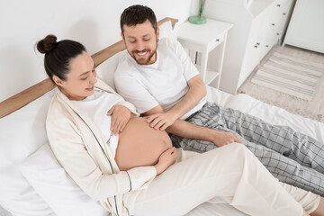Obraz premium Happy pregnant couple lying in bedroom