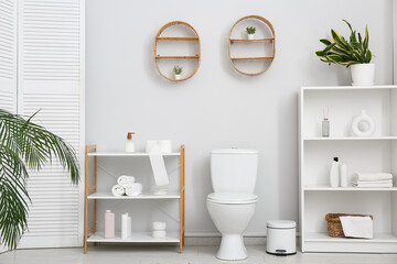 Stylish interior of light restroom with ceramic toilet bowl and bath supplies