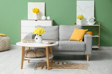 Cozy sofa with dresser, coffee table and narcissus flowers against green wall in living room