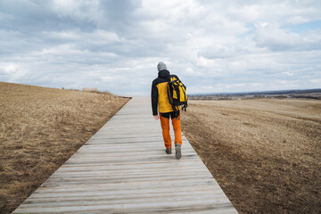 A person, casually carrying a comfortably packed backpack on their back, is leisurely walking along a scenic wooden path that beautifully winds its way through the serene beauty of nature