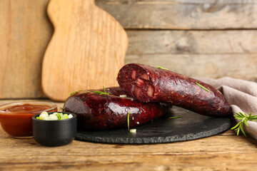 Tasty blood sausage, sauce and herbs on wooden background