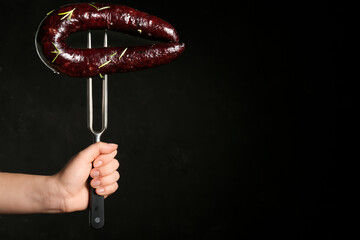 Hand holding meat fork with tasty blood sausage on dark background