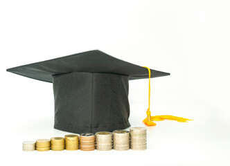 Graduation cap surrounded by stacks of coins isolate on white background.