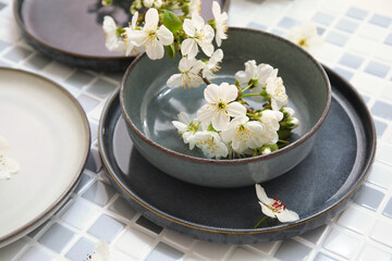 Different clean plates with blooming branch on grey tile background, closeup