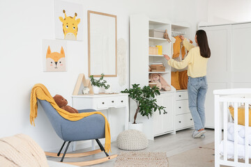 Young woman with hanging baby bodysuits in nursery, back view