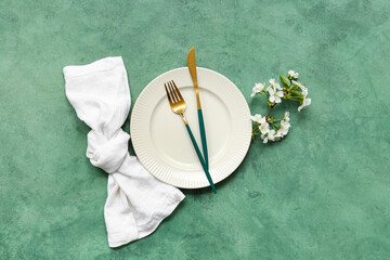 Fototapeta na wymiar Beautiful table setting with golden cutlery and blooming branch on green background