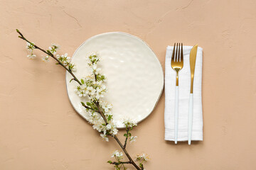 Beautiful table setting with golden cutlery and blooming branch on beige background