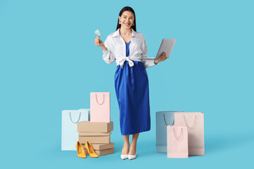 Happy young woman with laptop and credit card shopping online on blue background