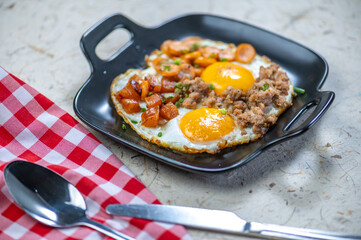 Hearty breakfast skillet with sunny side up eggs ground meat diced potatoes and fresh vegetables served in a black cast iron skillet on rustic surface