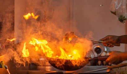 Man is cooking food in a kitchen with a lot of smoke and fire