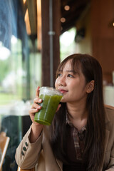young woman drinking green detox juice in cafe
