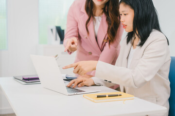 Two Asian businesswoman are engaged in a productive discussion at a modern office table, using a laptop and documents, exchanging ideas, and working together in a bright, professional environment