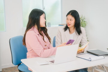 Obraz premium Two Asian businesswoman are engaged in a productive discussion at a modern office table, using a laptop and documents, exchanging ideas, and working together in a bright, professional environment