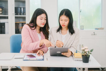 Two Asian businesswoman are engaged in a productive discussion at a modern office table, using a laptop and documents, exchanging ideas, and working together in a bright, professional environment