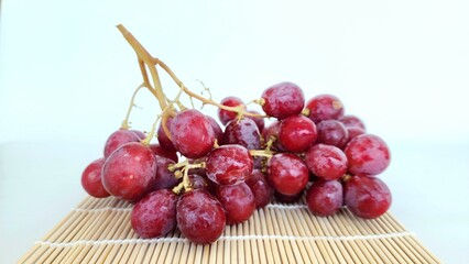 Red Globe grapes are a large seeded grape variety with a striking reddish red color and dense, crispy flesh on a woven bamboo base, isolated on white background