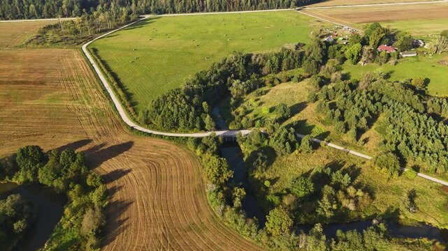 Winding river and farmland surrounded by trees near Tebras Upe in rural Latvia.