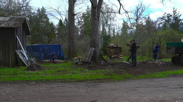 Fast-motion footage of people raking leaves and loading them onto a tractor during spring day at a Hageri countryside homestead, Estonia. Timelapse captures seasonal farm work and rural life teamwork