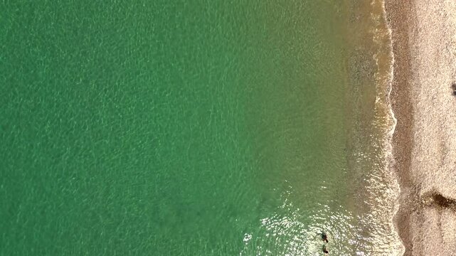 Aerial top view of beautiful coast line at Verga beach, Kalamata, two caucasian boys enjoying the crystal clear waters 4K