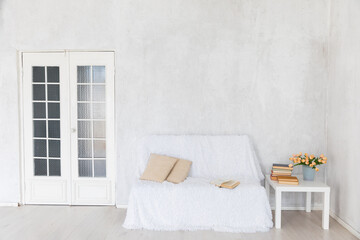 sofa and table with books and flowers in the interior of a white room