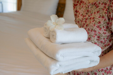 Hands of hotel maid putting plumeria flower and towels on the bed in the luxury hotel room ready for tourist travel