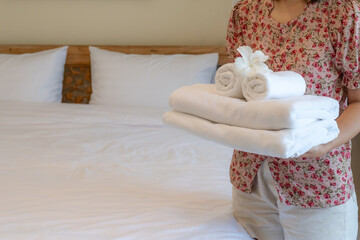 Hands of hotel maid putting plumeria flower and towels on the bed in the luxury hotel room ready for tourist travel