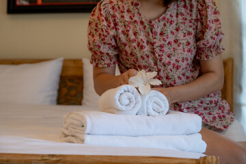 Hands of hotel maid putting plumeria flower and towels on the bed in the luxury hotel room ready for tourist travel.