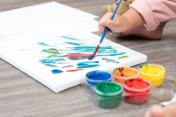 Close-up hand of toddler dipping paintbrush into red paint creating abstract strokes on white...