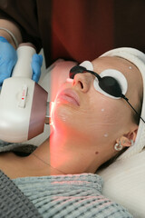 Beautiful young woman getting a facial treatment in a beauty clinic. Doctor uses photodynamic therapy for cosmetic procedures enhancing skin appearance