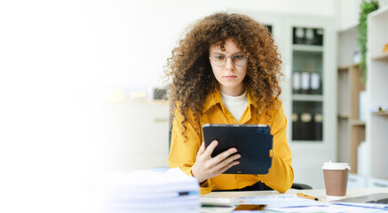 Obraz premium Confident businesswoman analyzing data on tablet at modern office desk with coffee, documents, and laptop. Concept of digital work