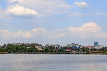 Obraz premium Scenic lakeside cityscape with urban buildings under fluffy clouds