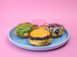 Colorful assorted donuts with vibrant icing and toppings on a blue plate, placed against a pink background