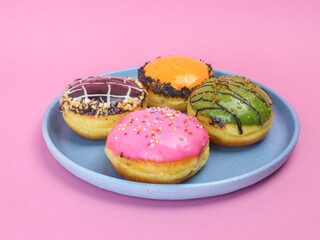 Colorful assorted donuts with vibrant icing and toppings on a blue plate, placed against a pink background