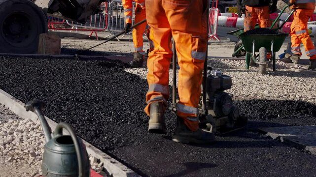Builders in bright orange uniforms laying fresh hot asphalt on construction site
