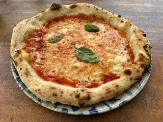 Freshly baked Margherita pizza topped with basil leaves served on a decorative plate