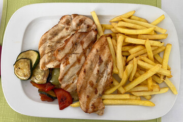 Grilled chicken breast served with crispy fries and mixed vegetables on a white plate