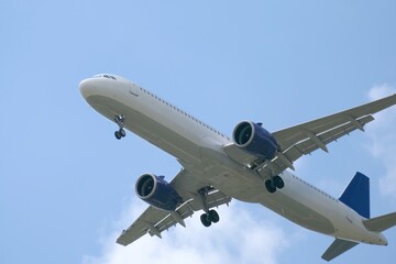 Commercial airplane flying over the city skyline during a clear day with blue skies and scattered clouds