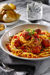 A plate of spaghetti and meatball perfectly placed on a marble countertop.