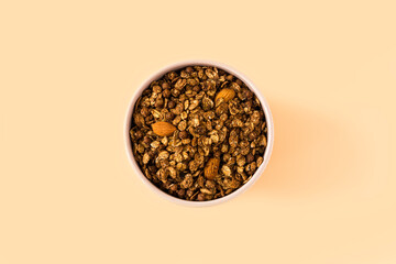 Top view of a ceramic bowl with chocolate granola on the light orange background , high-resolution . Muesli with chocolate and almonds close-up , place for text . 