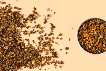 Top view of a ceramic bowl with chocolate granola on the light orange background , high-resolution . Muesli with chocolate and almonds close-up , place for text . 
